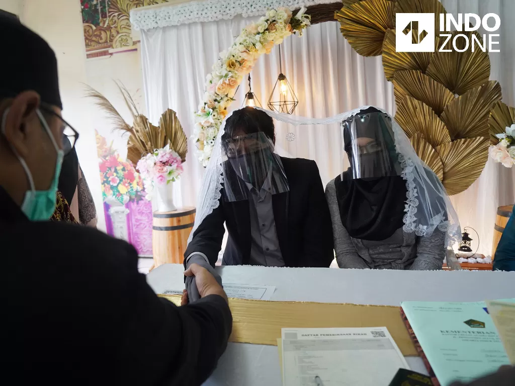  Pasangan pengantin Thomas Rudyanto (kiri) bersama Dian Larasati (kanan) menggunakan sarung tangan, masker, dan pelindung wajah saat melaksanakan prosesi akad nikah di KUA Ciracas, Jakarta, Sabtu (6/6/2020). (INDOZONE/Arya Manggala)