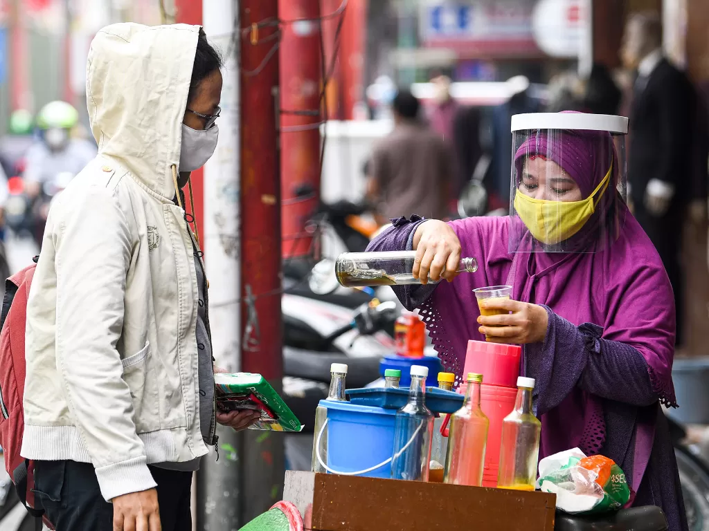 Penjual jamu keliling Tidar (kanan) dengan menggunakan masker dan pelindung wajah melayani pembeli di kawasan Pasar Baru, Jakarta, Selasa (9/6/2020). (ANTARA FOTO/M Risyal Hidayat)