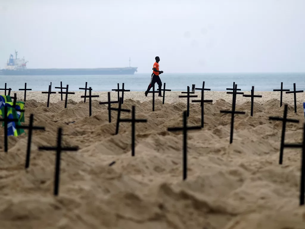 Seorang lelaki berlari melewati seratus kuburan yang digali oleh aktivis LSM Rio de Paz di pantai Copacabana yang melambangkan kematian akibat Covid-19, di Rio de Janeiro, Brasil, 11 Juni 2020. (REUTERS/Pilar Olivares)