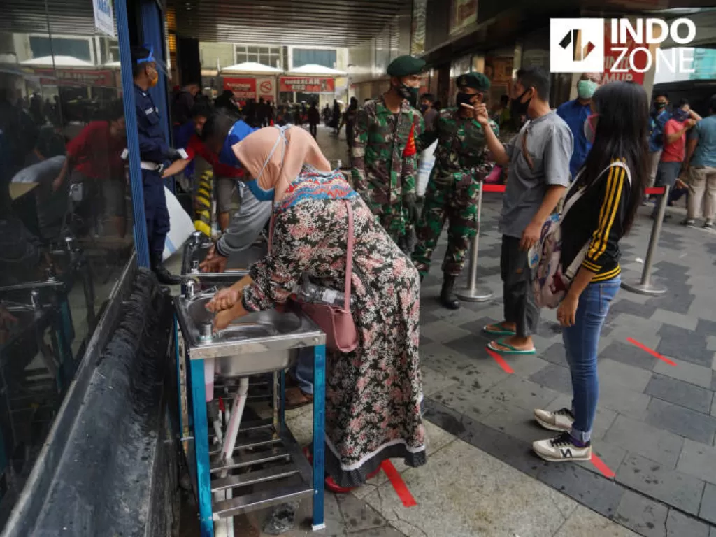 Pengunjung mengantre untuk mencuci tangan dan melakukan pemeriksaan suhu tubuh di pintu masuk Pasar Tanah Abang Blok A, Jakarta, Senin (15/6/2020). (INDOZONE/Arya Manggala)