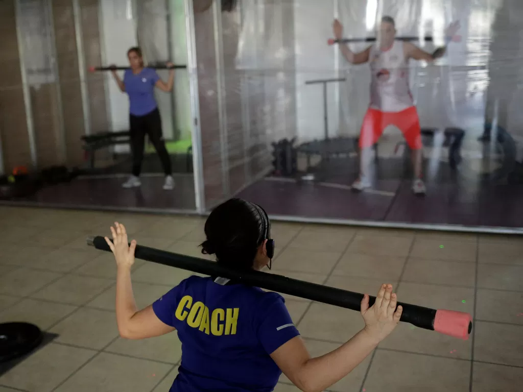 Seorang instruktur mengadakan kelas di gym yang memasang bilik plastik untuk menjaga jarak sosial di Ciudad Juarez, Meksiko 17 Juni 2020. (REUTERS/Jose Luis Gonzalez)