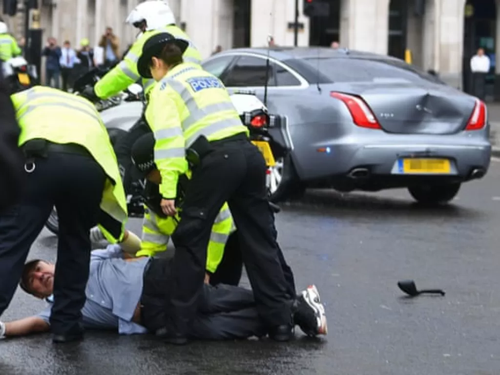 Tampilan mobil Jaguar XJ Sentinel milik PM Inggris yang hancur dan para demonstran yang sedang ditangkap polisi. (theguardian.com)