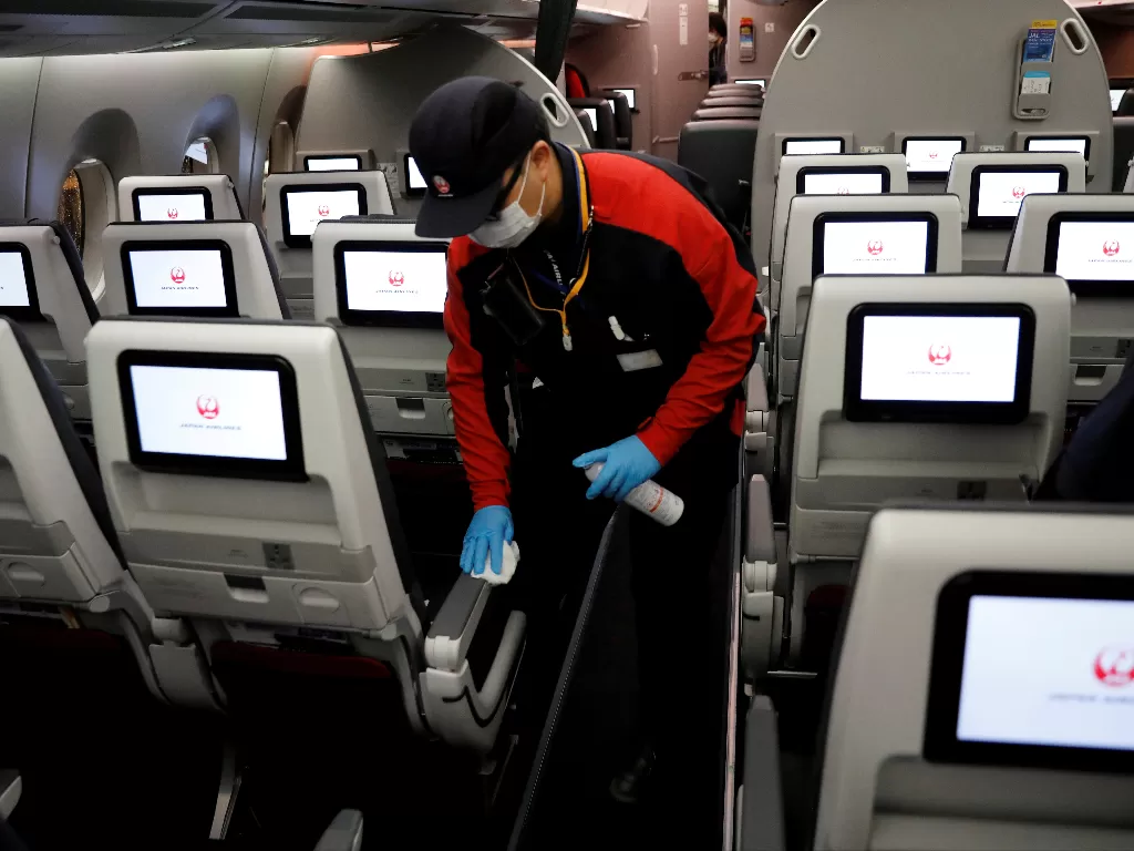 Seorang anggota staf Japan Airlines yang mengenakan masker wajah dan sarung tangan membersihkan kabin pesawat setelah melakukan penerbangan domestik. (Photo/REUTERS/Kim Kyung-Hoon)