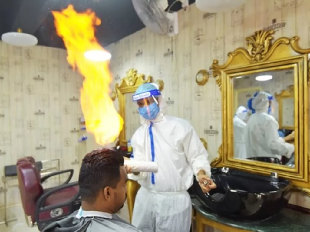 Seorang barber yang mengenakan alat pelindung diri menggunakan api untuk mencukur rambut di sebuah salon di Dhaka, Bangladesh, pada 23 Juni 2020. (Xinhua/Stringer)
