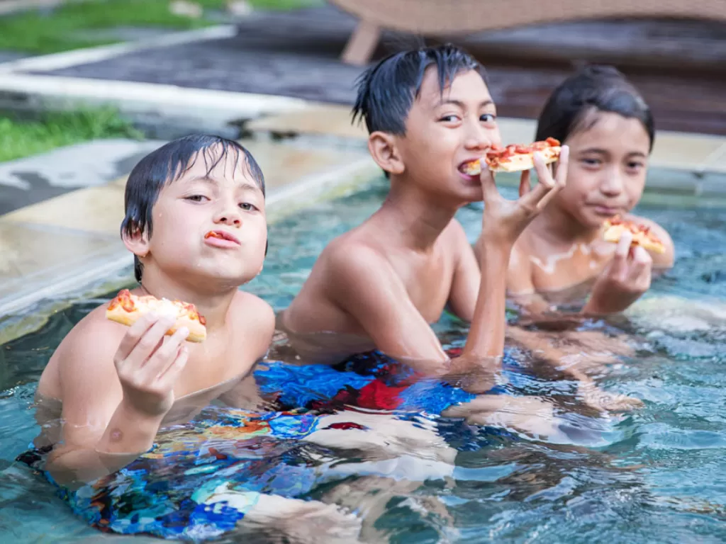 Potret nak-anak sedang makan pizza setelah berenang. (britannica.com)