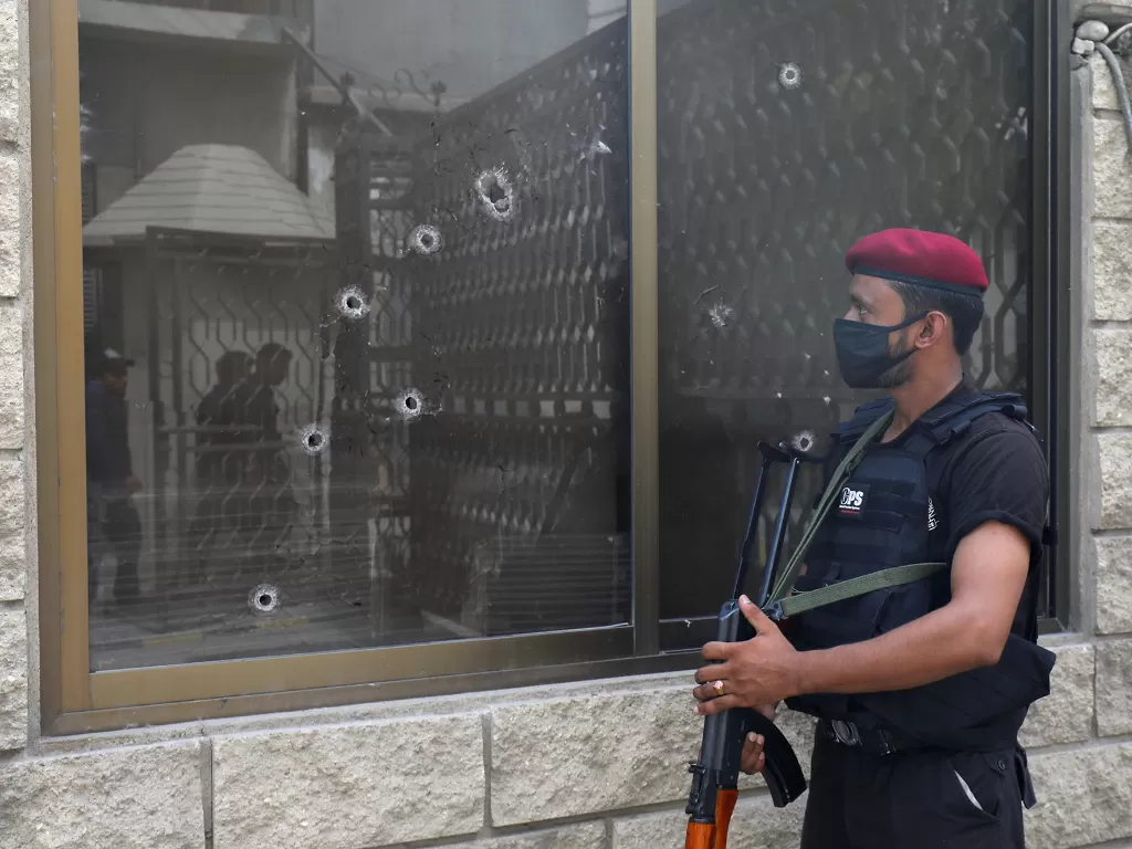 Seorang perwira polisi berjaga di samping jendela yang penuh peluru di gedung Bursa Efek Pakistan setelah serangan di Karachi, Pakistan 29 Juni 2020. (REUTERS/Akhtar Soomro)