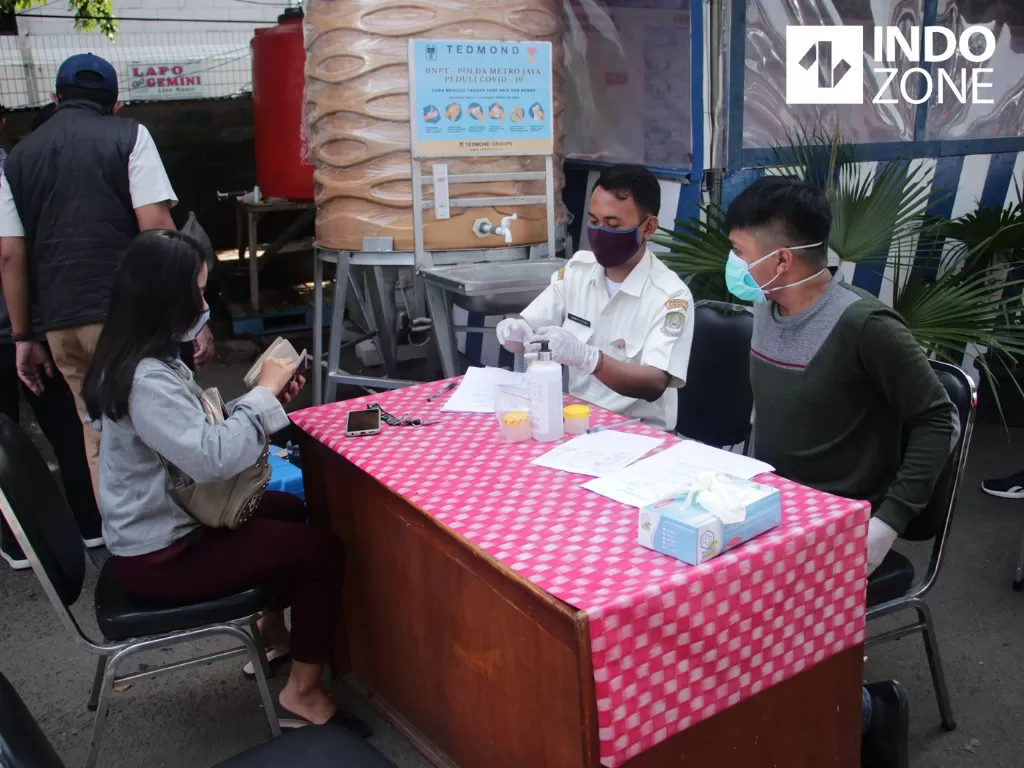 Petugas Dinas Kesehatan Bekasi Kota mendata warga yang akan melakukan tes PCR (Polymerase Chain Reaction) di Check Point Sumber Artha, Bekasi, Jawa Barat. (INDOZONE/Febio Hernanto)