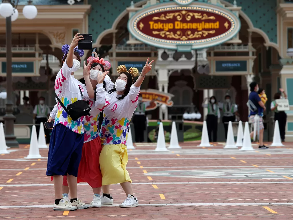 Pengunjung berswafoto saat pembukaan kembali Disneyland dan DisneySea Tokyo, yang ditutup selama berbulan-bulan karena Covid-19, di Urayasu, timur Tokyo, Jepang 1 Juli 2020. (REUTERS/Issei Kato)