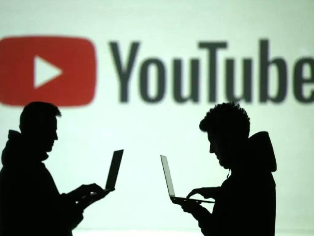 Ilustrasi pengguna perangkat seluler di sebelah proyeksi logo Youtube (photo/Reuters/Dado Ruvic/Illustration)