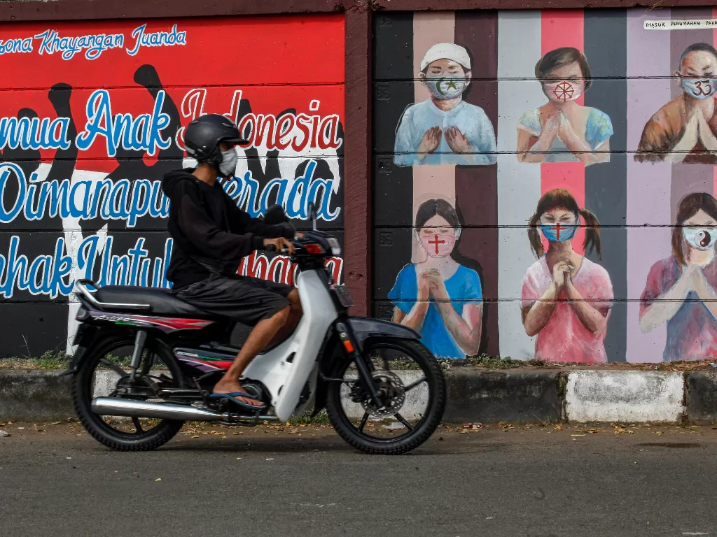 Ilustrasi - Pengendara sepeda motor melintas di dekat mural bergambar simbol orang berdoa menggunakan masker. (Photo/Ilustrasi/ANTARA FOTO/Yulius Satria Wijaya)