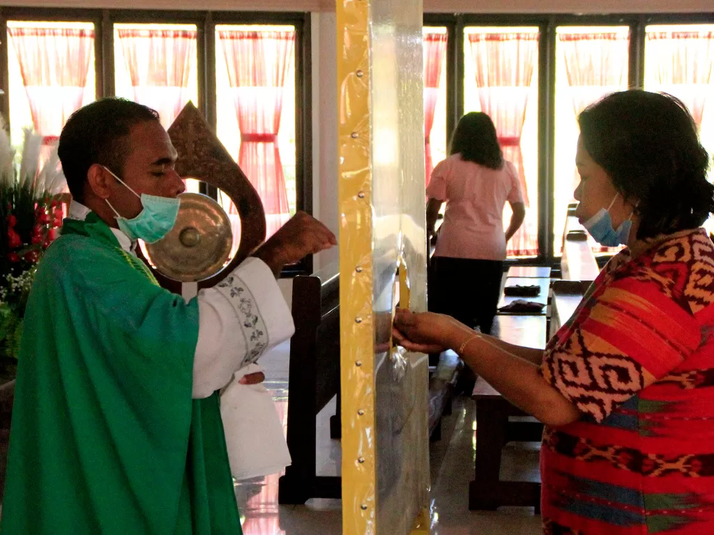 Seorang pastor menggunakan masker dan pembatas membagikan hosti kepada umat Katolik yang melaksanakan ibadah hari Minggu di gereja Santo Gregorius Agung Oeleta di Kota Kupang, NTT,Minggu (5/7/2020). (ANTARA FOTO/Kornelis Kaha)