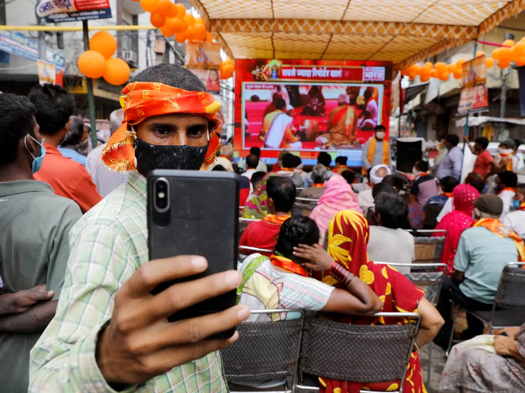 Seorang warga hindu mengenakan masker pelindung wajah saat swafoto berlatar belakang layar monitor yang sedang menyiarkan acara peresmian Ram Temple secara virtual oleh Perdana Menteri Narendra Modi di Ayodhya, New Delhi, India (5/8/2020). (Photo/REUTERS/