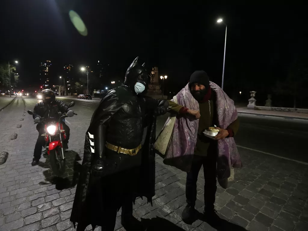 Seorang pria yang tak mau disebutkan namanya memakai kostum Batman membagikan makanan kepada tunawisma.(photo/REUTERS/Ivan Alvarado)