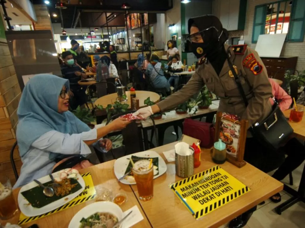 Petugas kepolisian membagikan masker kepada pengunjung restoran. (ANTARA FOTO/Oky Lukmansyah)