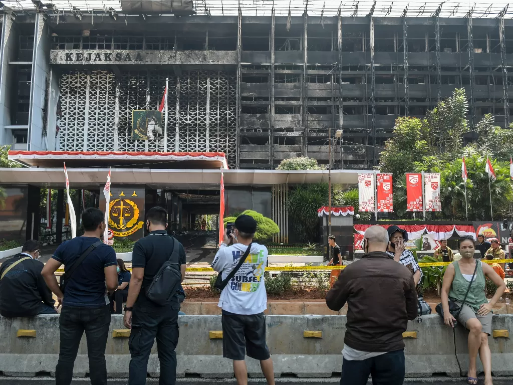 Warga menyaksikan petugas pemadam kebakaran melakukan proses pendinginan di gedung utama Kejaksaan Agung yang terbakar di Jakarta, Minggu (23/8/2020). (ANTARA FOTO/Galih Pradipta)