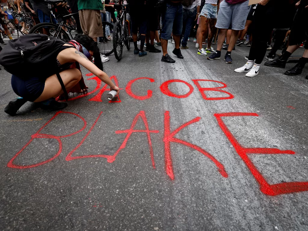 Seorang wanita melukis nama pria kulit hitam Jacob Blake di jalan ketika pengunjuk rasa menunjukkan kesetaraan rasial di tengah kota Manhattan menyusul penembakan polisi di Wisconsin of Blake, di New York City (REUTERS/MIKE SEGAR)