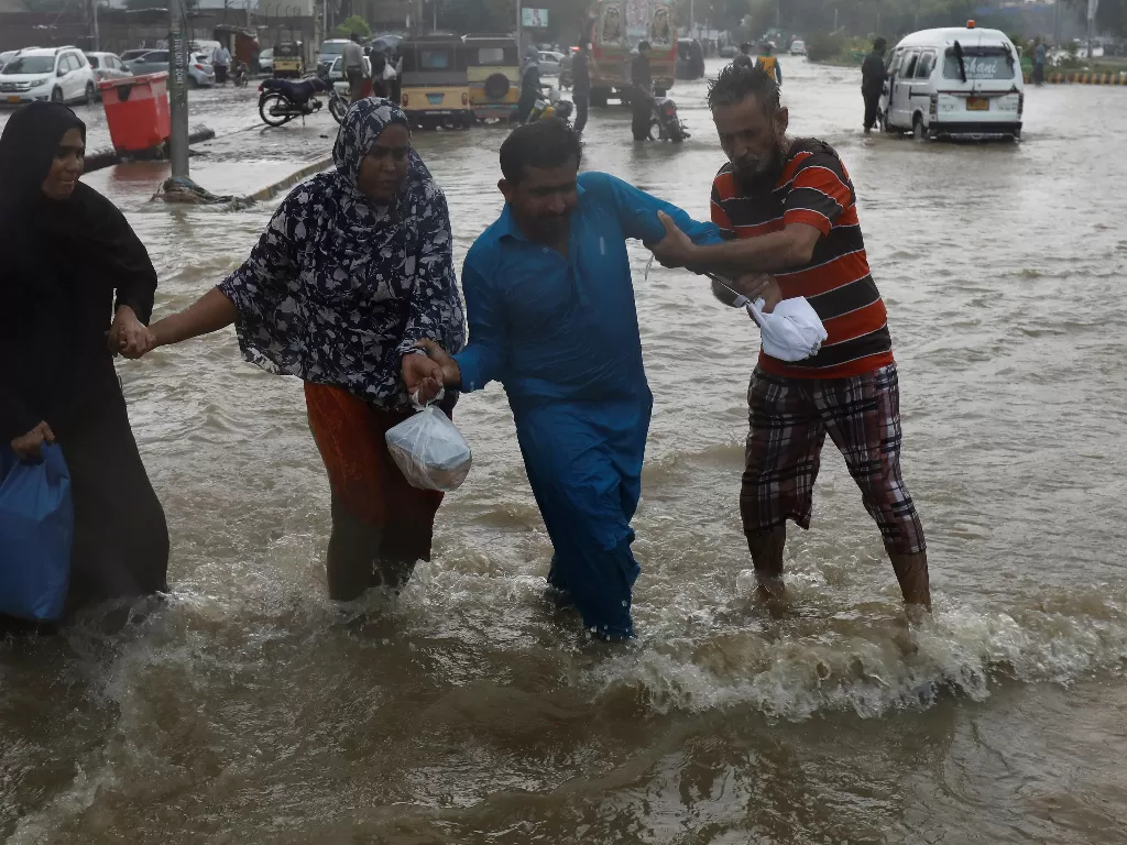 Orang-orang saling membantu saat mereka mengontrol keseimbangan melalui jalan yang banjir (REUTERS/AKHTAR SOOMRO)