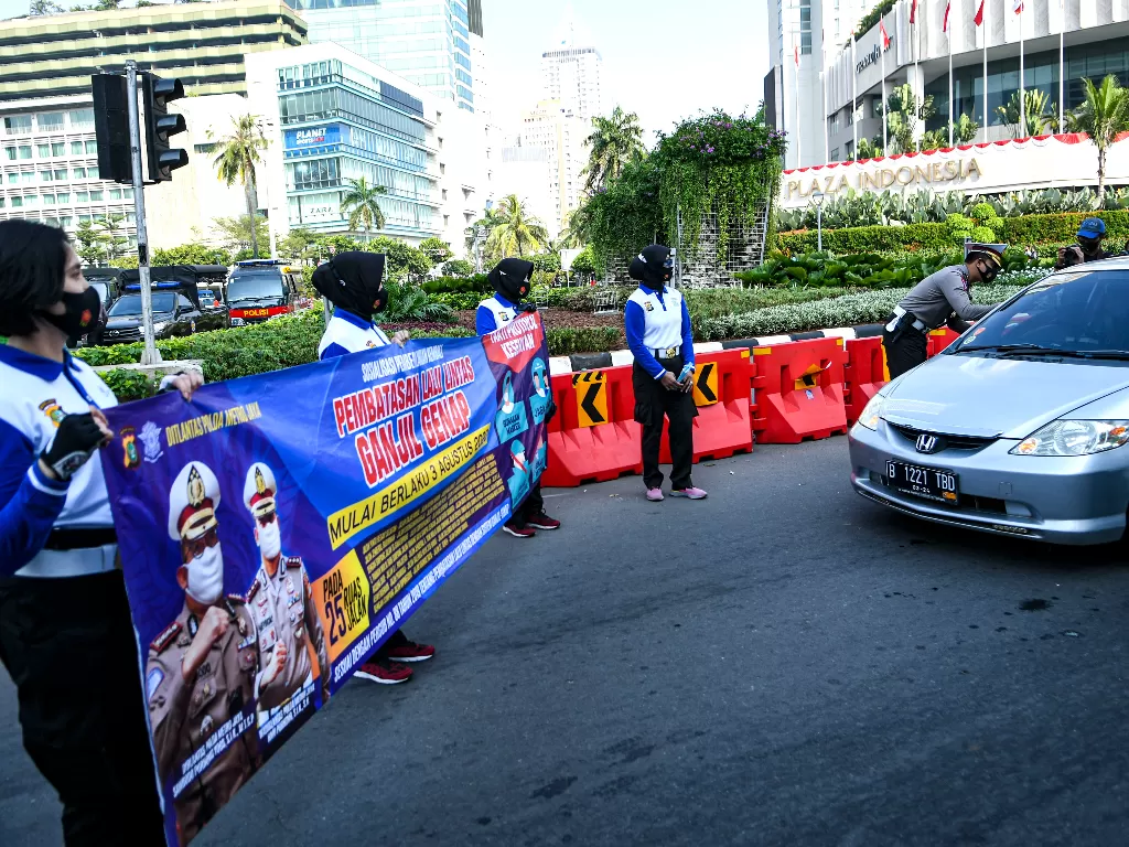 Sejumlah anggota Kepolisian membentangkan spanduk sosialisasi pemberlakuan kembali ganjil genap di Bundaran Hotel Indonesia, Jakarta, Minggu (2/8/2020). (ANTARA FOTO/M Risyal Hidayat)