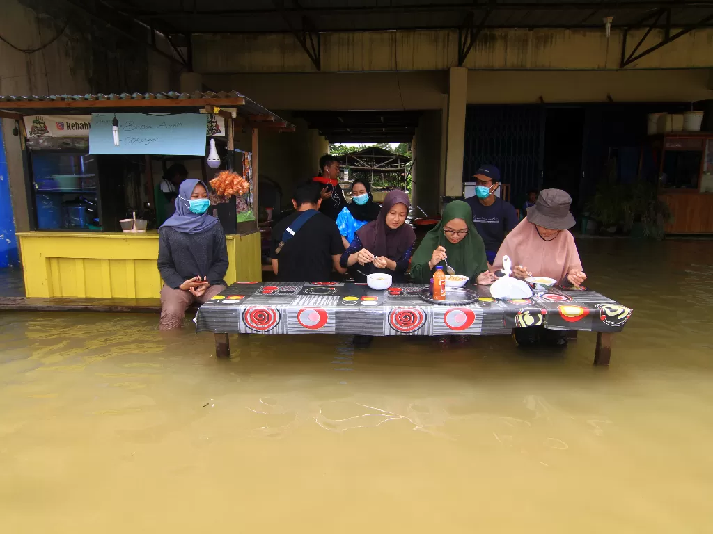 Sejumlah warga menyantap makanan di sebuah warung yang terendam banjir di Putussibau, Kabupaten Kapuas Hulu, Kalimantan Barat, Selasa (15/9/2020). ANTARA FOTO/Jessica Helena Wuysang