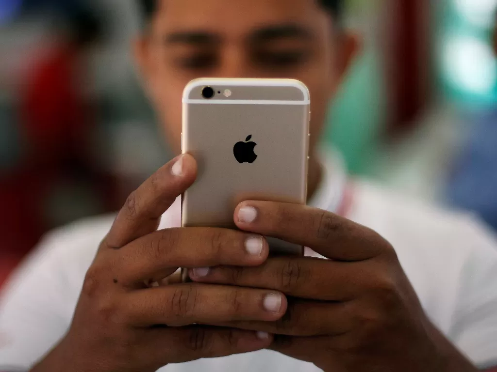 Seorang pria sedang memegang smartphone iPhone di New Delhi, India (photo/REUTERS/Adnan Abidi)