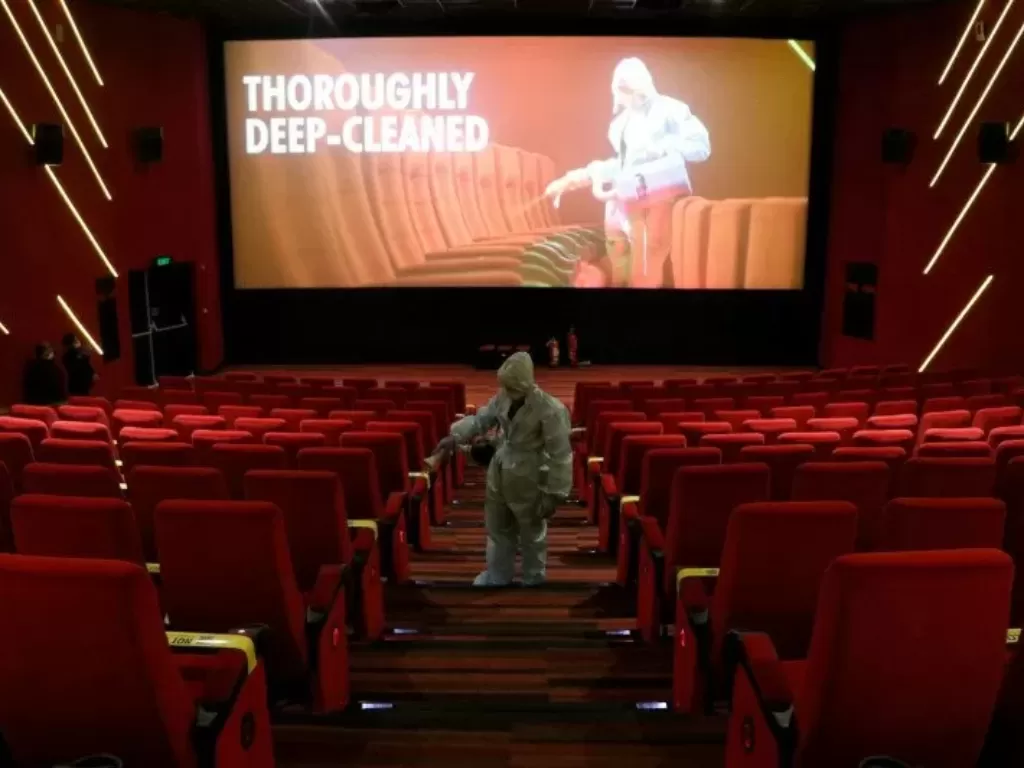 Seorang petugas memakai alat pelindung diri (APD) membersihkan tempat duduk di dalam bioskop. (Photo/REUTERS/NIHARIKA KULKARNI)