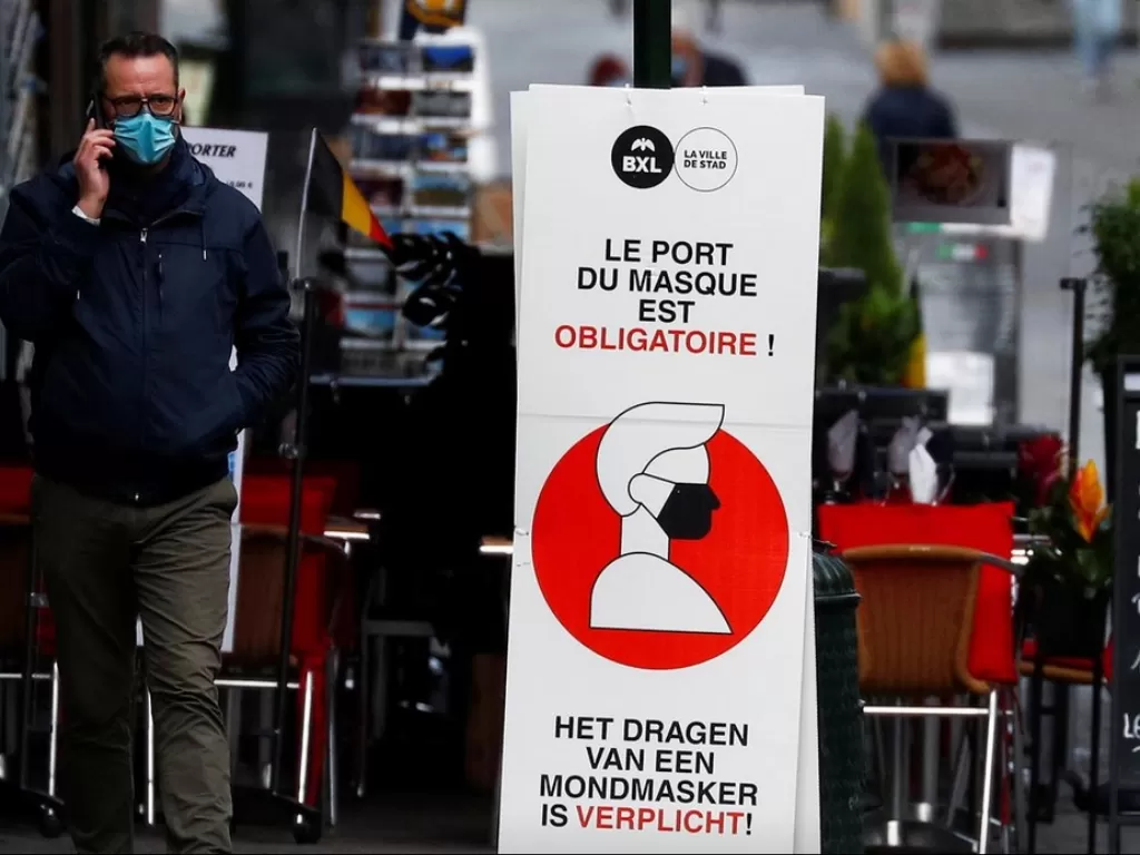 Seorang pria berjalan di samping tanda wajib menggunakan masker di Brussels, Belgia, Jumat (16/10/2020). (REUTERS/Francois Lenoir)