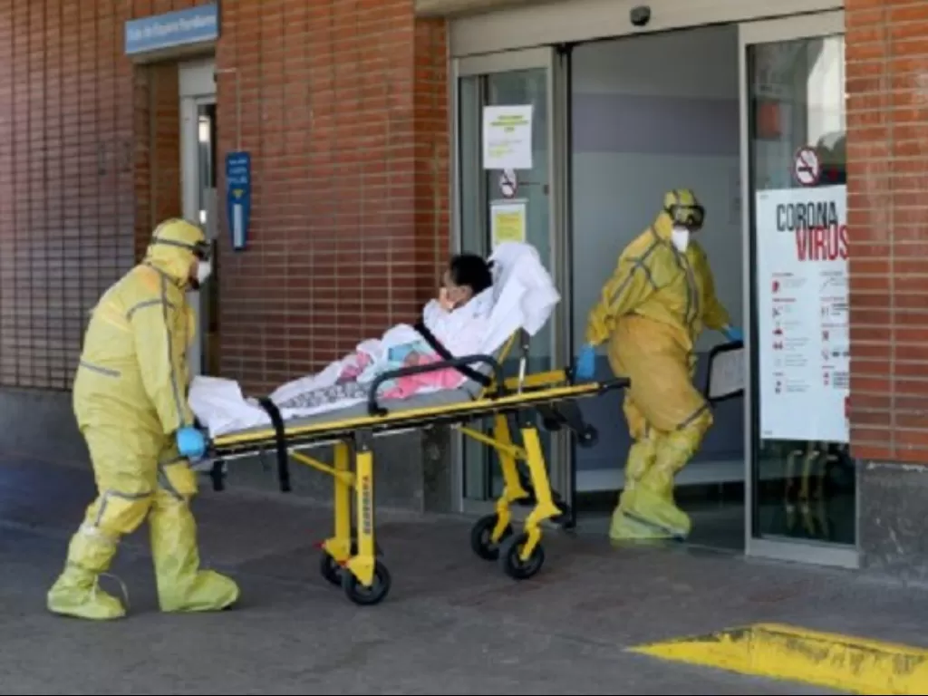 Petugas ambulans dengan pakaian pelindung tiba bersama seorang pasien di Rumah Sakit Severo Ochoa di tengah wabah virus corona (COVID-19) di Leganes, Spanyol, Kamis (26/3/2020). (REUTERS/Susana Vera)