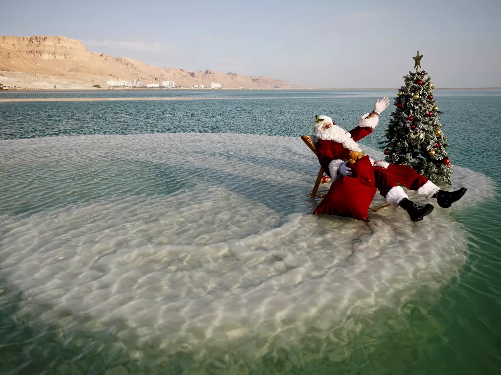 Issa Kassissieh, mengenakan kostum Santa Claus, duduk di samping pohon Natal di atas formasi garam di Laut Mati (REUTERS/Amir Cohen)