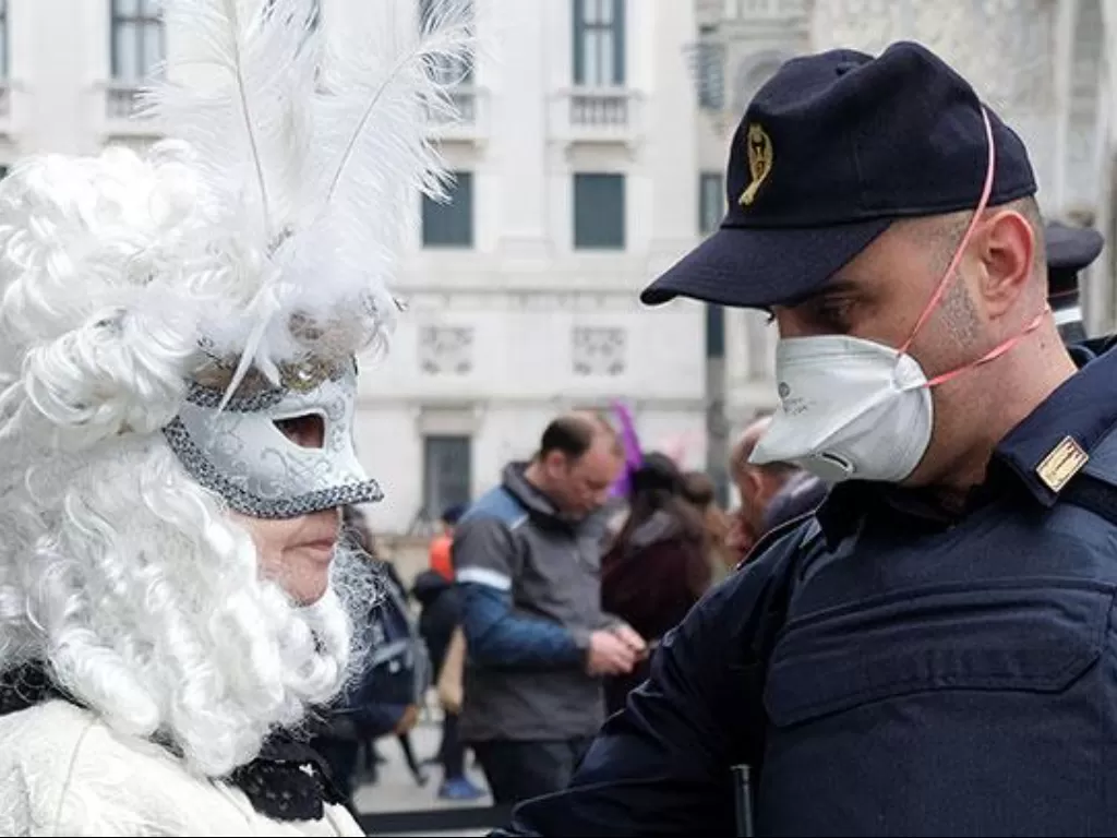 Polisi mengenakan masker pelindung saat berbicara dengan seorang pengunjung berkostum di Venice Carnival di Venesia, Italia, (23/2/2020). (REUTERS/Manuel Silvestri)