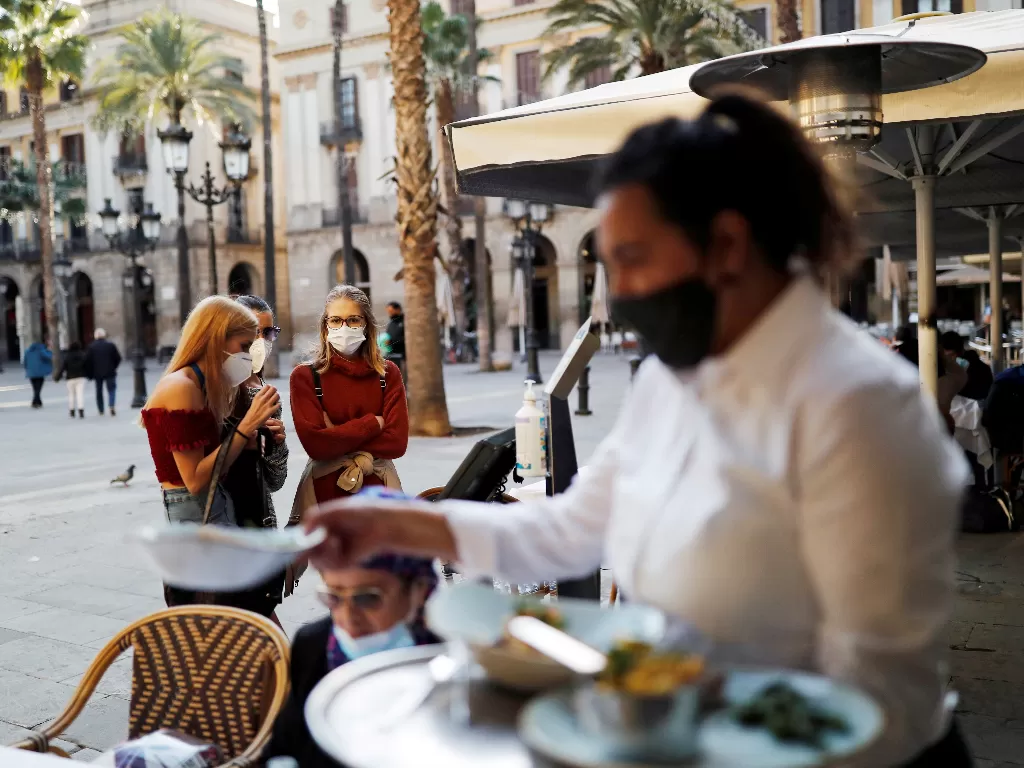 Orang-orang yang memakai masker wajah menunggu di teras restoran Les Quinze Nits di alun-alun (REUTERS/Nacho Doce)