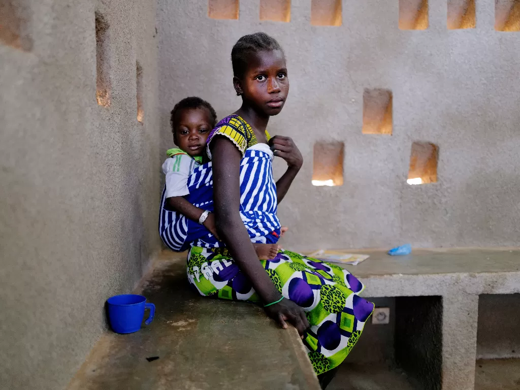 Zonabo Sore, 11, yang melarikan diri dari serangan militan bersenjata di wilayah Sahel menggendong keponakannya yang berusia enam belas bulan, Housein, yang menderita malnutrisi (REUTERS/Zohra Bensemra)