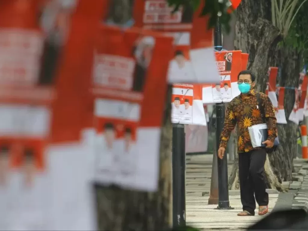 Warga melintas di trotoar yang dipasangi alat peraga kampanye (APK) salah satu pasangan calon Wali Kota dan Wakil Wali Kota Surabaya di Jalan Dharmawangsa, Surabaya, Jawa Timur, Senin (30/11/2020). (Photo/Ilustrasi/ANTARA FOTO/Moch Asim)