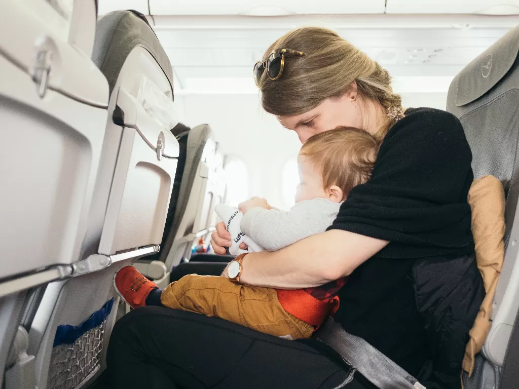 Ilustrasi seorang ibu membawa bayinya dalam pesawat. (Unsplash/@plhnk)