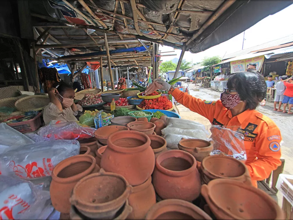 Personel Badan Penanggulangan Bencana Daerah (BPBD) membagikan masker kepada pedagang di Pasar induk Indramayu, Jawa Barat, Jumat (18/12/2020). (Photo/ANTARA FOTO/Dedhez Anggara)