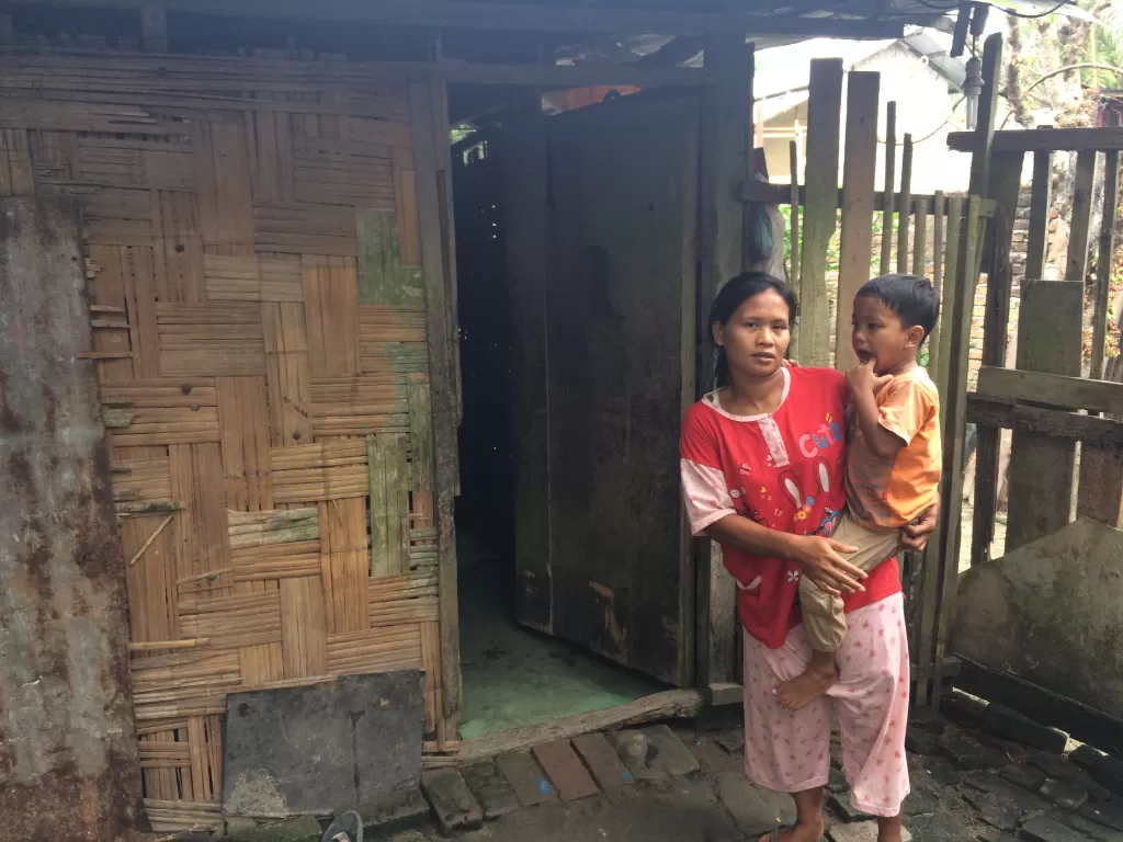 Eva Agustina menggendong anak bungsunya di depan rumah gubuknya di Desa Citaman Jernih, Perbaungan, Serdangbedagai. (Indozone.id/Abul Muamar)