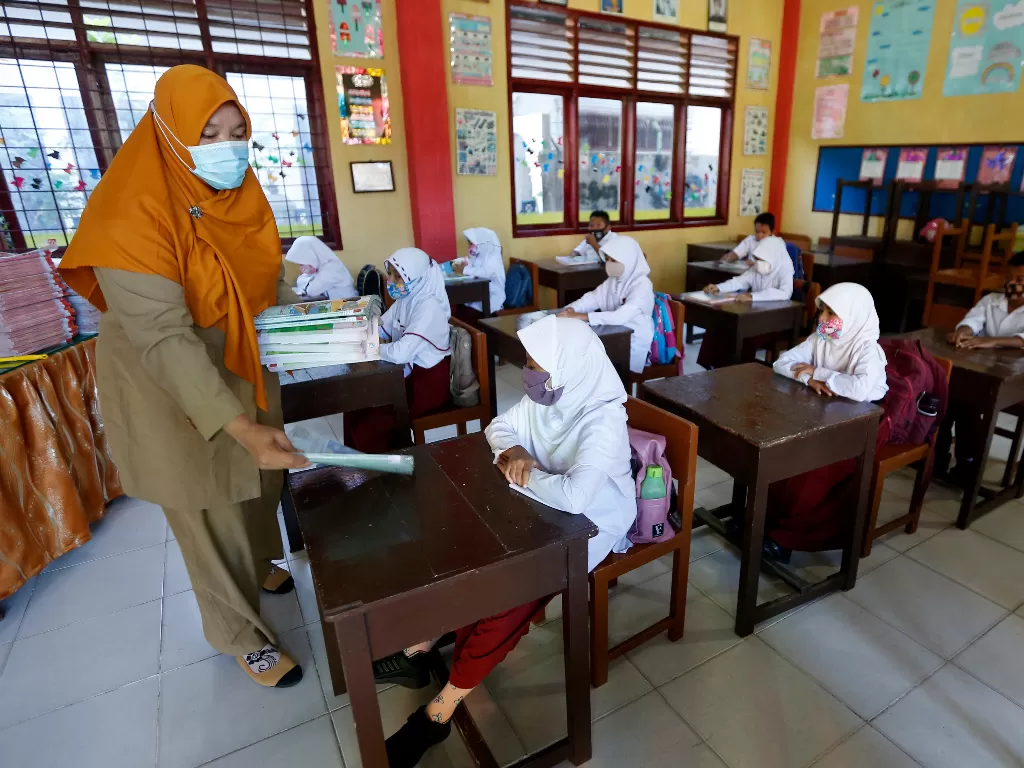 Guru membagikan buku pelajaran kepada pelajar pada hari pertama sekolah tatap muka di SD Negeri 42, Banda Aceh, Aceh, Senin (4/1/2021)