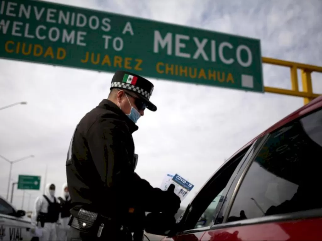 Petugas polisi membagikan brosur berisi informasi tentang Covid-19 kepada orang yang masuk ke Meksiko dari AS di Ciudad Juarez, Meksiko, Minggu(29/3/2020). (REUTERS/Jose Luis Gonzalez)