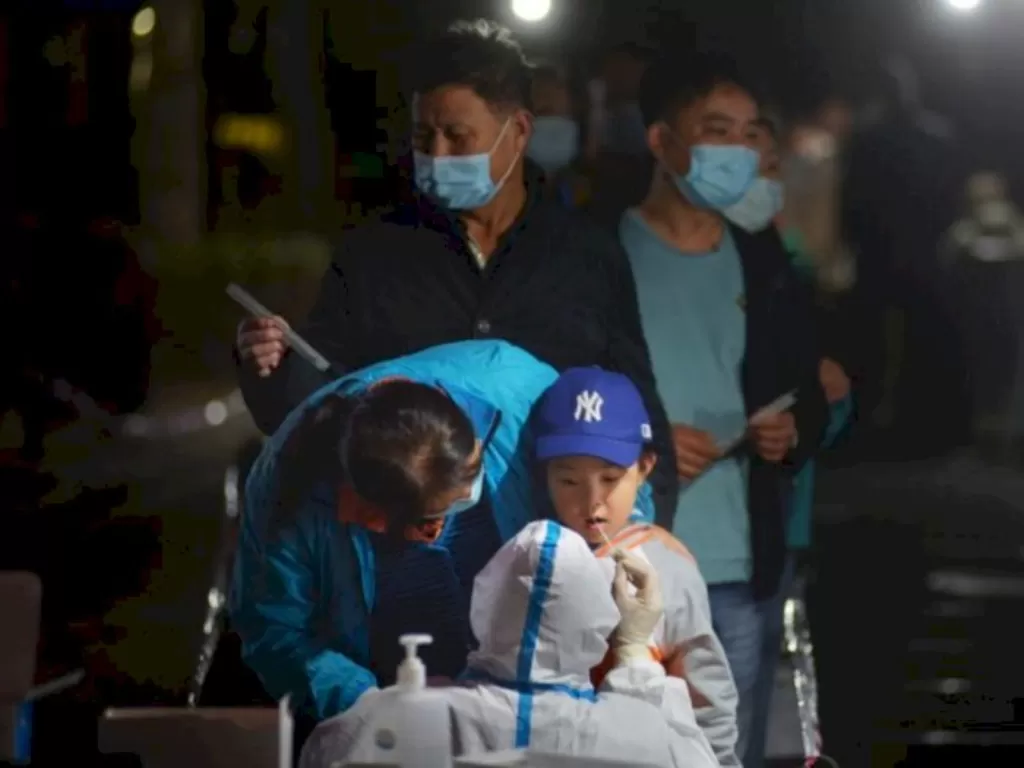Petugas kesehatan dengan baju hazmat melakukan tes swab Covid-19 pada seorang anak laki-laki di Qingdao, Shandong, Tiongkok, Selasa (13/10/2020). (REUTERS/cnsphoto)