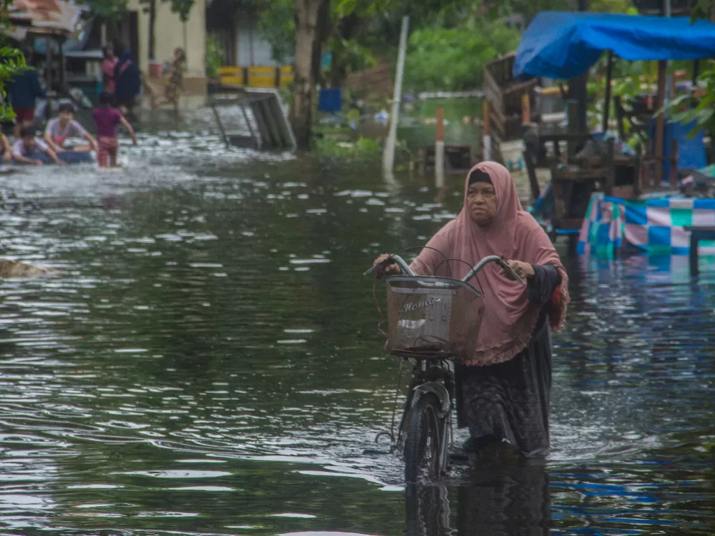 Warga menuntun sepedanya melintasi banjir yang merendam Jalan Prona di Banjarmasin, Kalimantan Selatan, Kamis (14/1/2021). (ANTARA/Bayu Pratama)