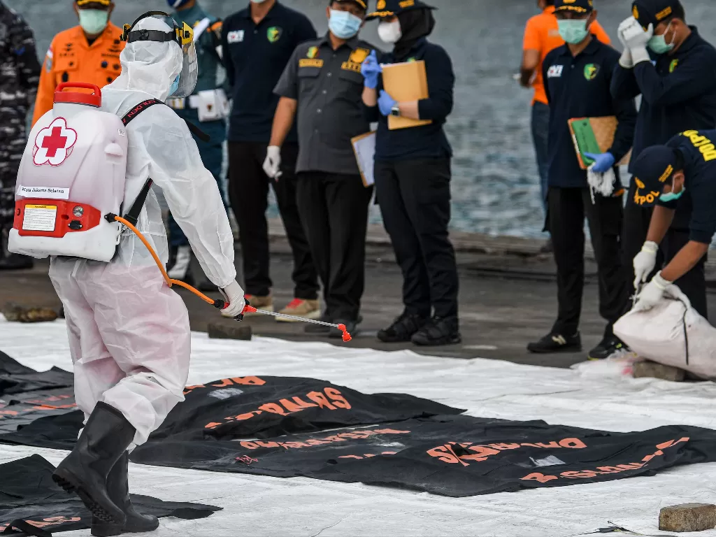 Petugas PMI menyemprotkan cairan disinfektan ke kantong jenazah berisi objek temuan dari lokasi jatuhnya pesawat Sriwijaya Air. (Foto: ANTARA/M Risyal Hidayat)