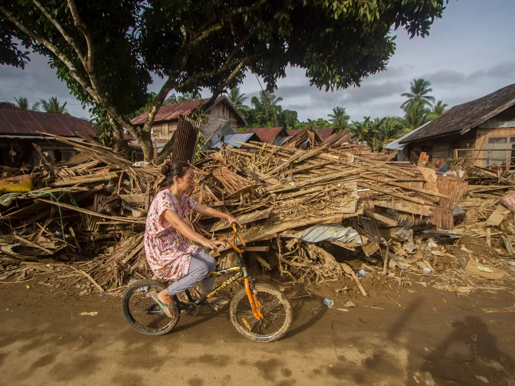 Warga menggunakan sepeda melintas di dekat puing-puing rumah akibat banjir bandang di Desa Waki (ANTARA FOTO/Bayu Pratama S)