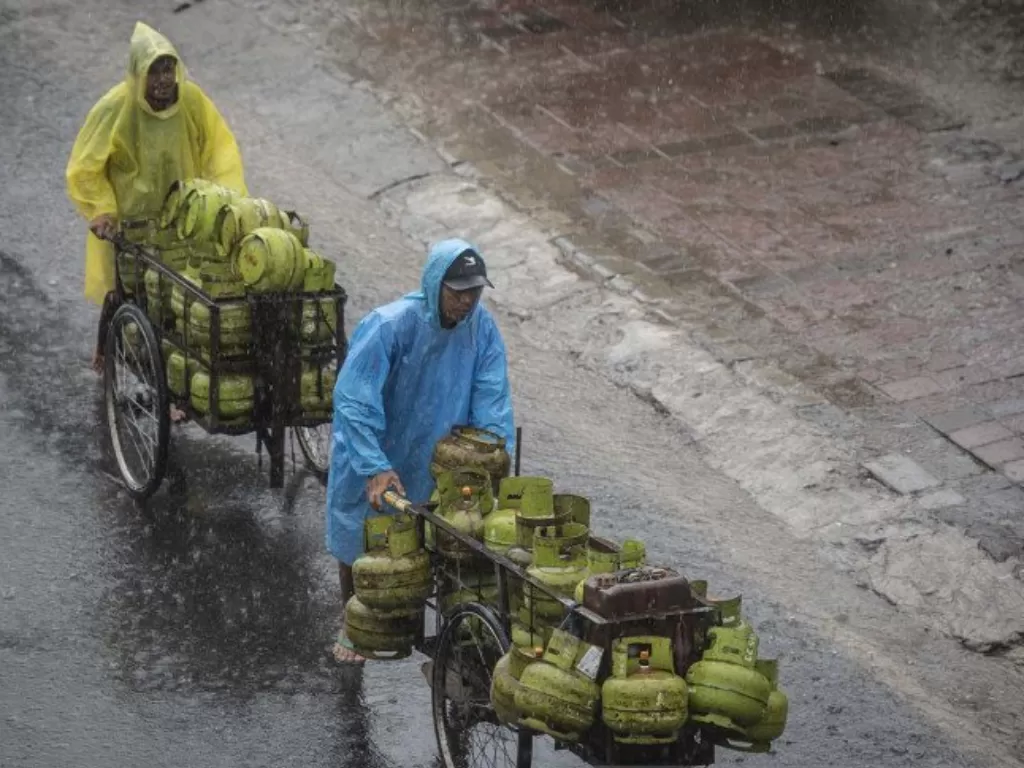 Pedagang mendorong gerobak berisi tabung LPG saat hujan di Jalan KH Mas Mansyur, Tanah Abang, Jakarta, Selasa (26/1/2021). (ANTARA FOTO/Aprillio Akbar)