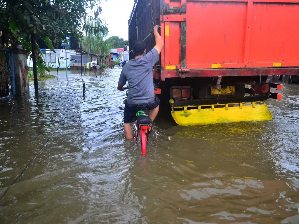 Warga menaiki sepeda berpegangan truk saat menerobos banjir yang menggenangi jalan. (Foto: ANTARA/Yusuf Nugroho)
