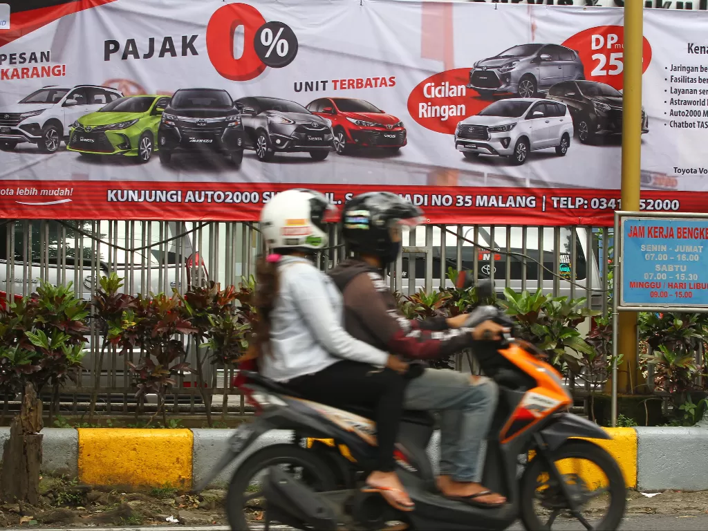  Pengendara motor melintas di depan spanduk yang memuat materi promosi pembelian mobil dengan relaksasi Pajak Penjualan Atas Barang Mewah (PPnBM) di depan diler Toyota Auto2000, Malang, Jawa Timur, Senin (1/3/2021). (ANTARA FOTO/Ari Bowo Sucipto)