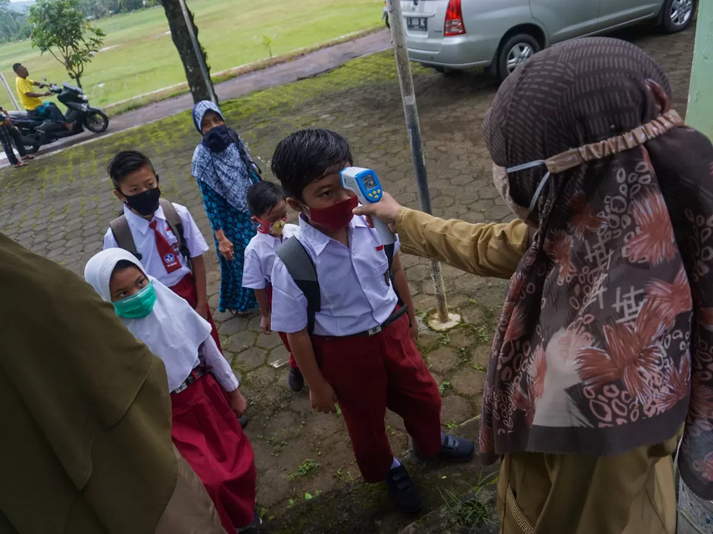 Guru mengecek suhu tubuh siswa saat memasuki SD N Simbangdesa 1, Tulis, Kabupaten Batang, Jawa Tengah, Selasa (9/3/2021).(ANTARA FOTO/Harviyan Perdana Putra)