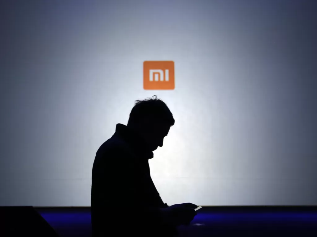 Siluet seorang pria sedang berdiri di depan logo Xiaomi (photo/REUTERS/Jason Lee)
