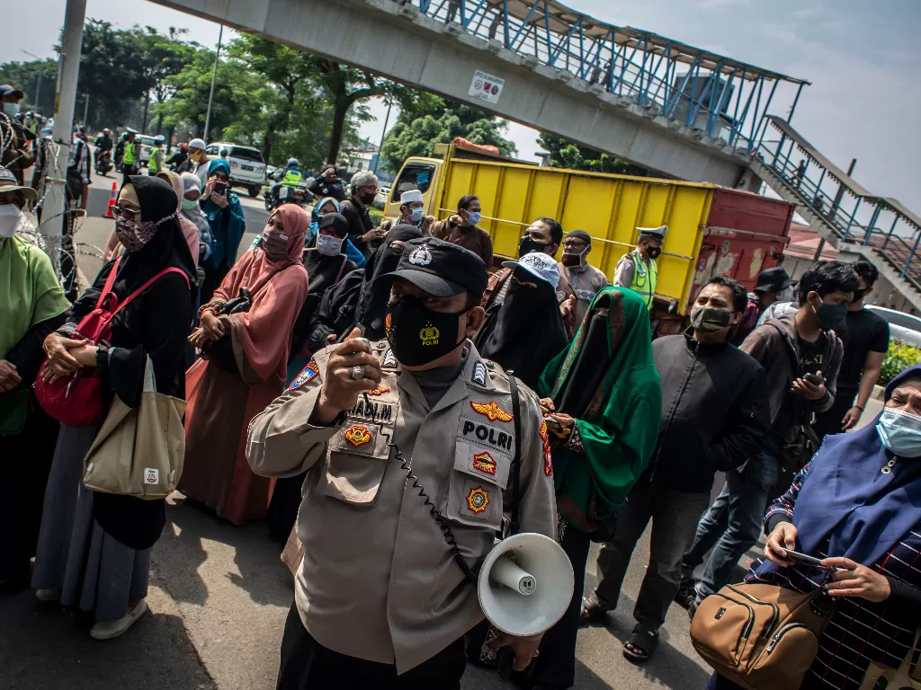 Petugas Kepolisian mengimbau kepada massa pendukung untuk menjaga jarak saat berlangsungnya sidang lanjutan kasus pelanggaran protokol kesehatan dengan terdakwa Rizieq Shihab di PN Jakarta Timur. (Foto: ANTARA/Aprillio Akbar)