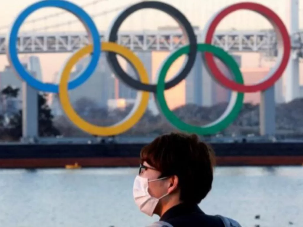  Ilustrasi: Seorang pria mengenakan masker sedang berdiri di depan logo Olimpiade di Jepang. (REUTERS) 