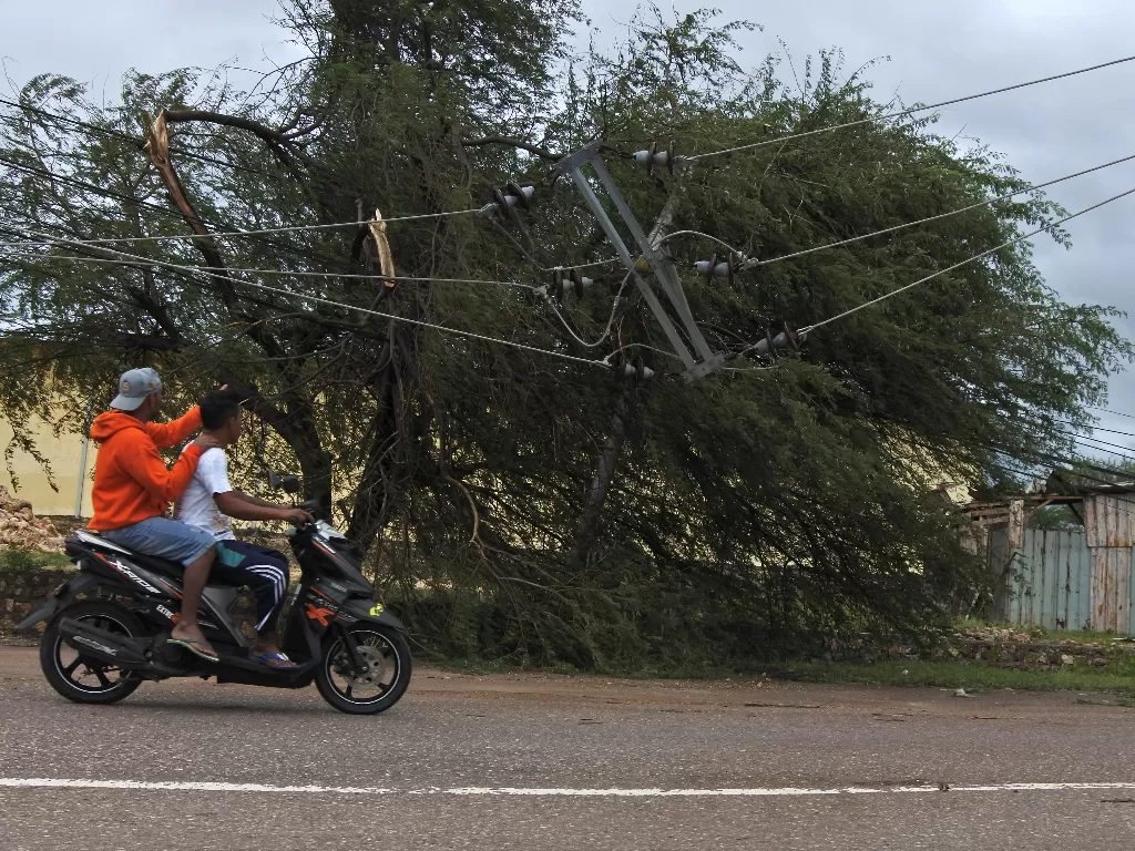 Pengendara motor melintas di samping tiang listrik yang patah akibat diterjang angin kencang di Kota Kupang, NTT, Senin (5/4/2021). (ANTARA/Kornelius Kaha)