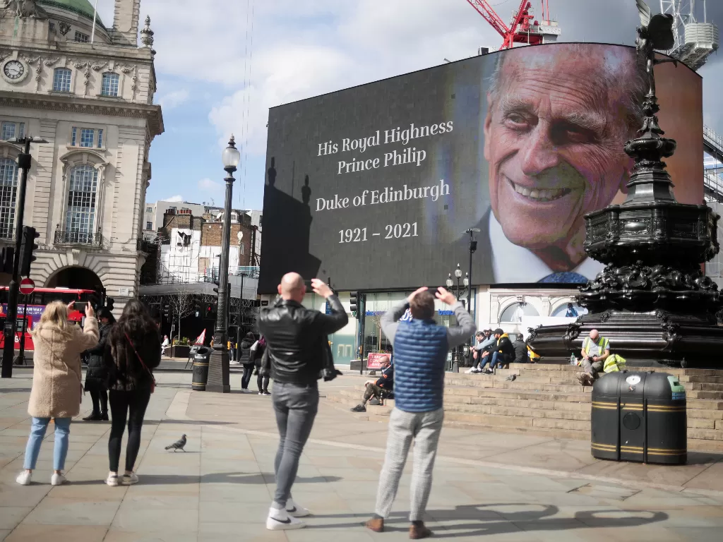 Orang-orang mengambil gambar layar dengan gambar dan pesan tentang Pangeran Philip dari Inggris, suami Ratu Elizabeth, setelah dia meninggal pada usia 99, di London, Inggris, 9 April 2021. (photo/REUTERS/Hannah McKay)